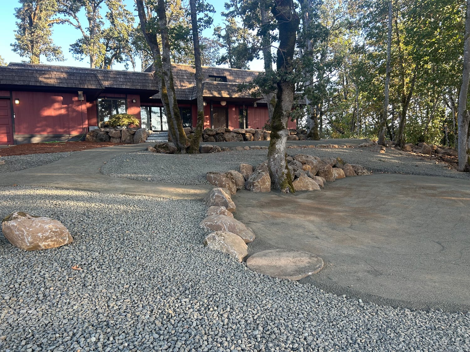 Boulder wall curving around the trees on a finished gravel drive.